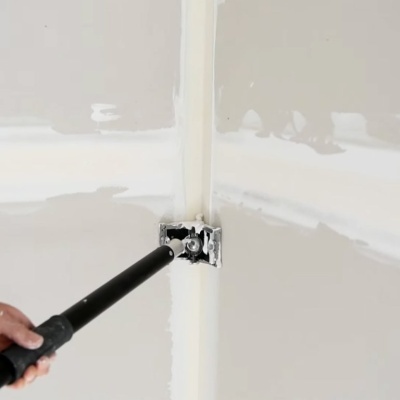 Aplicação de massa para juntas com tubo preto em cantos de paredes brancas.