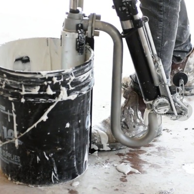 balde preto com manchas de tinta branca ao lado de equipamento metálico e calças manchadas