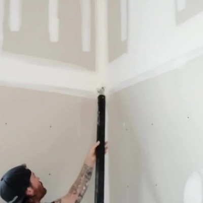 Homem a aplicar massa em paredes e tetos com aplicador longo, instruções em português e marca Columbia