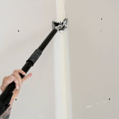 Dispositivo preto aplicando pintura branca entre duas paredes brancas