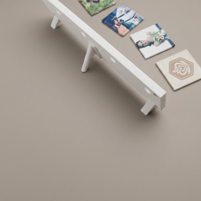 Base branca para azulejos com cinco furos e suportes, ao lado de azulejos decorativos coloridos em superfície cinza.