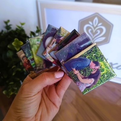 Pequenos blocos de chocolates com fotografias coloridas em mão sobre chão de madeira com planta ao fundo.