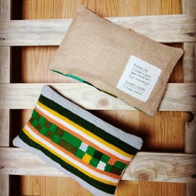 Dois sacos pequenos, um de juta bege com rótulo e outro de crochê colorido sobre madeira clara