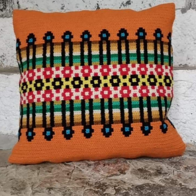 Almofada tricotada com padrão colorido sobre superfície de pedra