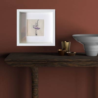 Moldura branca com ilustração de bailarino rosa, sobre mesa de madeira com tigela cinzenta e recipientes metálicos dourados