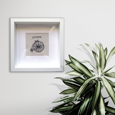 Quadro com ilustração de bicicleta e texto LET'S RIDE na parede ao lado de planta