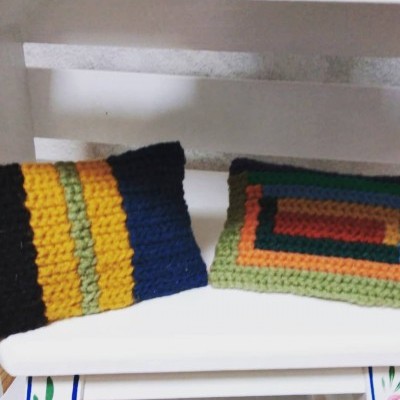 Duas almofadas tricotadas coloridas sobre banco branco com detalhes pintados