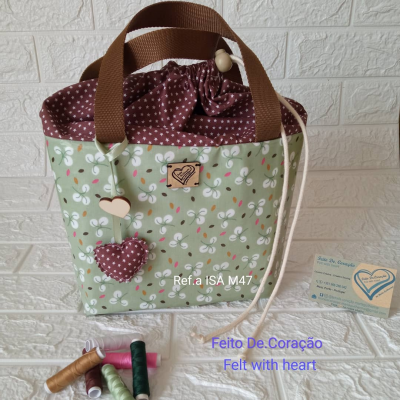 Bolsa de tecido floral verde com detalhes castanhos e pingentes em forma de coração, com linhas coloridas à frente
