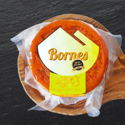 Queijo redondo alaranjado embalado a vácuo com etiqueta Bornes numa tábua de madeira