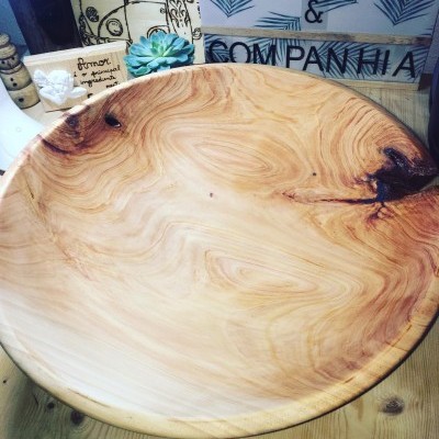 Prato raso grande de madeira com padrões naturais sobre mesa de madeira e decoração ao fundo