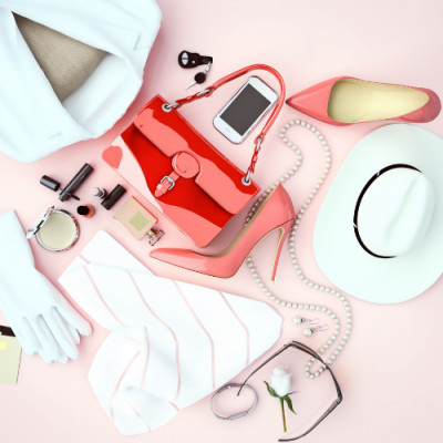 Acessórios femininos sobre fundo rosa, incluindo mala vermelha, sapatos cor-de-rosa e chapéu branco