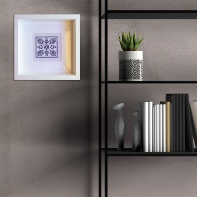 Estante preta com livros, esculturas cinzas, vaso branco com padrão preto e planta, parede cinza com quadro branco e bordado roxo