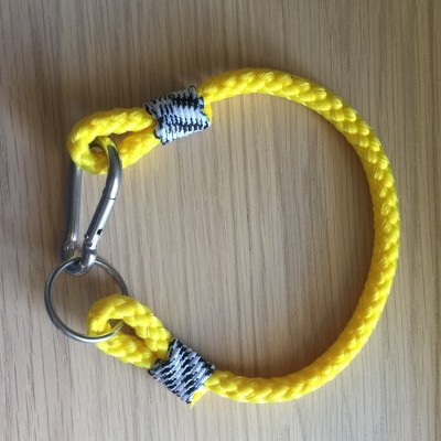 Pulseira de corda amarela com mosquetão e argola metálica sobre madeira clara