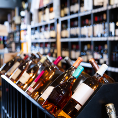 Garrafa de vinho com cápsulas coloridas e rótulos brancos em prateleira numa loja