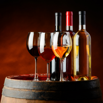 Três garrafas de vinho e três copos de vinho tinto, rosé e branco sobre barril de madeira com fundo castanho.