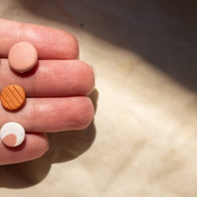 Seis pares de brincos redondos coloridos exibidos na mão sobre fundo claro