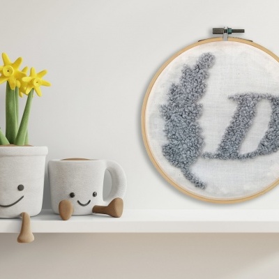 Vasos de cerâmica com rostos e flores amarelas ao lado de bordado com letra D numa prateleira branca