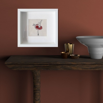 Mesa de madeira escura com copos dourados, prato cinzento ondulado e quadro com bordado de bailarina