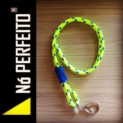 Trela amarela com padrão verde com gancho metálico sobre madeira, texto NÓ PERFEITO no lado