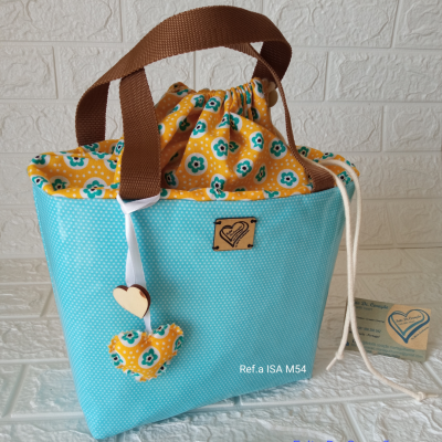 Bolsa artesanal azul e amarela com padrão floral e bolinhas, alças castanhas e ornamentos decorativos.