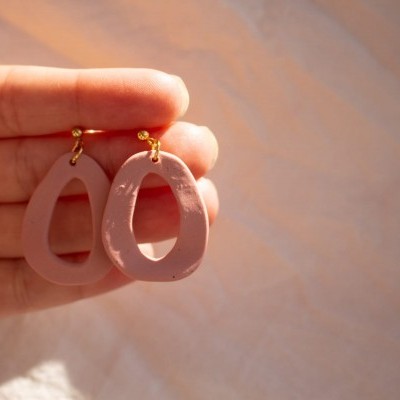 Brincos pendentes em acrílico rosa com argolas douradas na mão