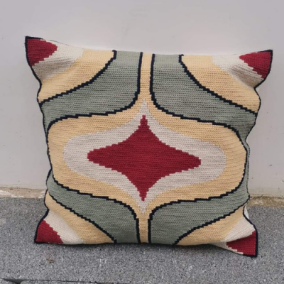 Almofada de tecido com padrão geométrico colorido em tons de vermelho, bege, cinza e preto