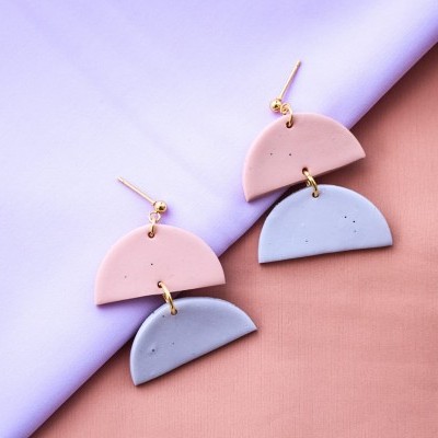 Brincos pendentes de semi-círculos rosas e cinzentos sobre tecido lilás e castanho