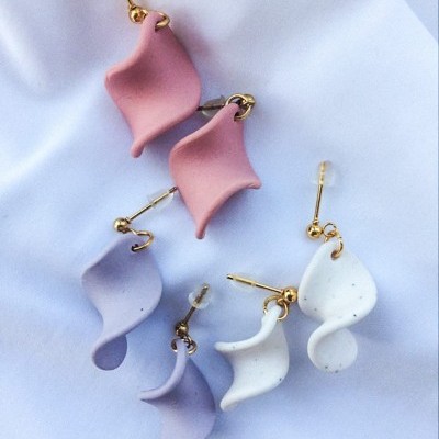 Brincos pendentes coloridos sobre tecido branco.