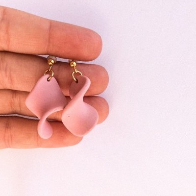 Brincos rosa claro ondulados sendo segurados por uma mão