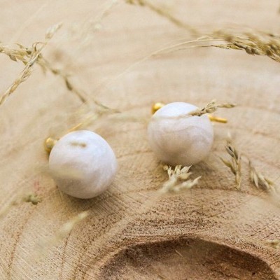 Brincos com pedras brancas e detalhes dourados sobre madeira com ramos secos