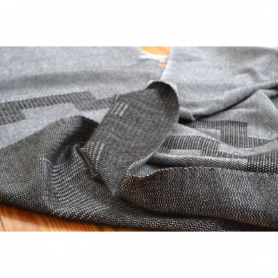 Peça de vestuário cinzenta com padrão geométrico sobre superfície de madeira