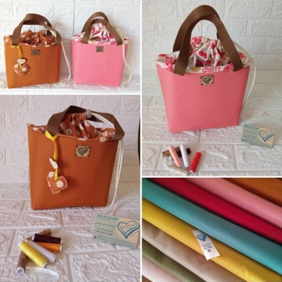 Malas de tecido laranja e rosa com alças castanhas e forro estampado, tecidos coloridos e rolos de linha num fundo branco.