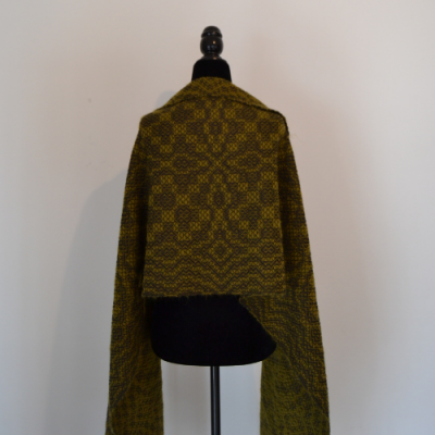 Xale amarelo com padrão geométrico num manequim preto contra parede branca