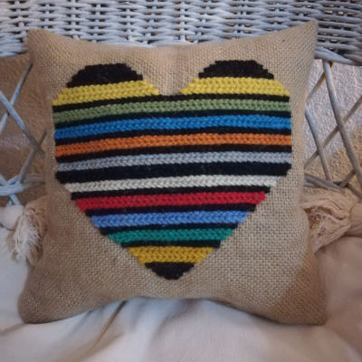 Almofada bege com coração colorido em crochet numa cadeira de vime branca