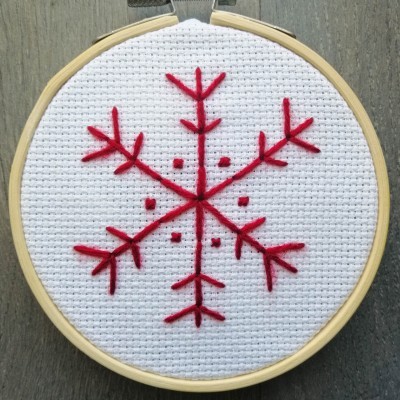 Bastidor de madeira com bordado de floco de neve vermelho em tecido branco