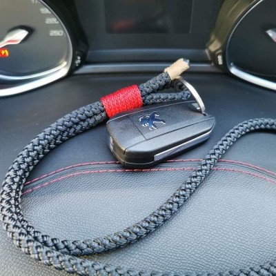 Chave Peugeot preta com cordão trançado sobre painel de carro preto com costuras vermelhas