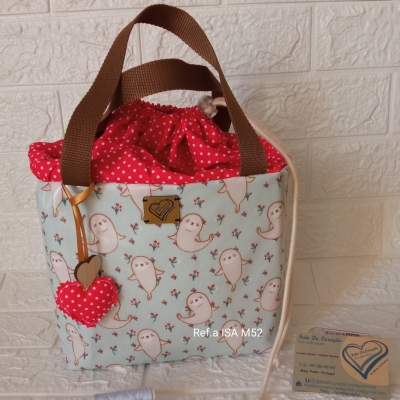 Bolsa de tecido com padrão de fantasmas e flores, alças castanhas e fecho de cordão vermelho