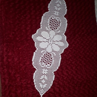 Caminho de mesa branco em renda com flores e corações sobre tecido vermelho texturizado.