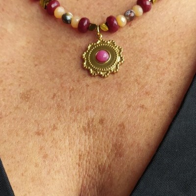Colar de contas coloridas com pendente dourado e vermelho no pescoço.