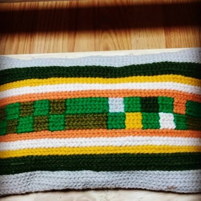 Almofada têxtil retangular com padrão geométrico colorido sobre madeira clara