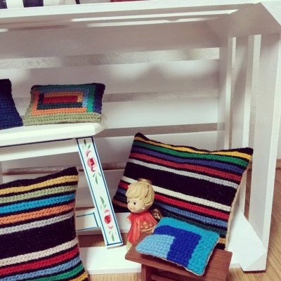 Almofadas tricotadas coloridas num móvel branco com figura decorativa e banco de madeira pequeno