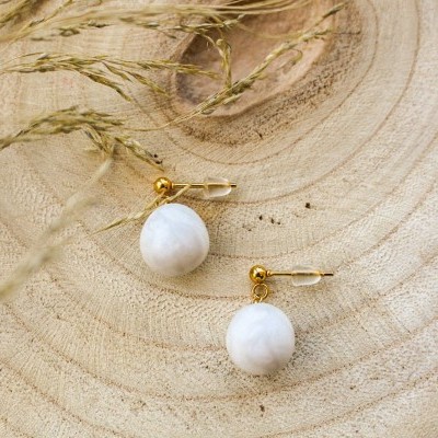 Brincos com bola branca texturizada em gancho dourado sobre madeira e ramos secos