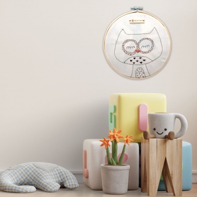 Bastidor com bordado de coruja, cubos coloridos, vaso com flores, almofada e caneca sorridente