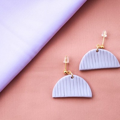 Brincos semicirculares lilás com detalhes dourados em fundo rosa