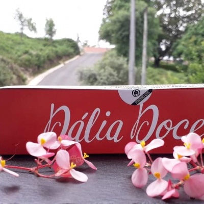 Caixa vermelha Dália Doce cercada de flores rosas com cenário natural ao fundo