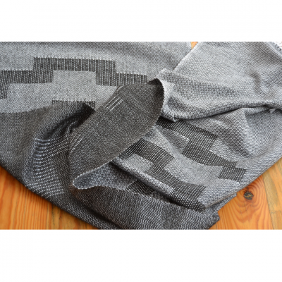 Lenço ou echarpe cinzento com padrão geométrico sobre superfície de madeira.