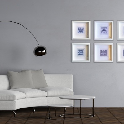 Sala com sofá cinzento, lâmpada preta e quadros brancos com padrões azuis na parede.