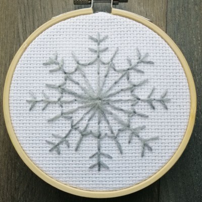 Bastidor com tecido branco e bordado cinzento em padrão de floco de neve