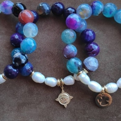 Colares coloridos com contas facetadas, pérolas brancas e pingentes dourados sobre fundo castanho.