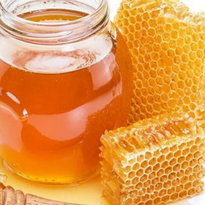 Frasco de mel com favos de mel ao lado e colher de mel